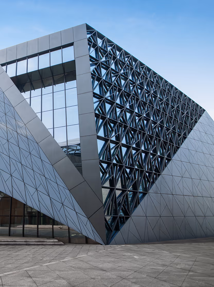Modern building facade with angular geometric panels and a patterned window section under a clear blue sky.
