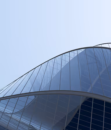 Close-up of modern building's curved glass facade reflecting a clear blue sky.